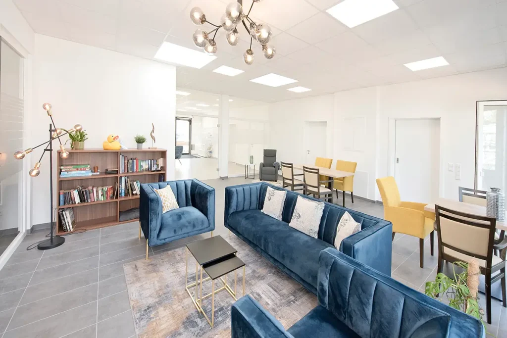 Einladender Aufenthaltsbereich mit blauen Sofas, Bücherregal und Leseecke bei Pensum MED Gärtringen.
