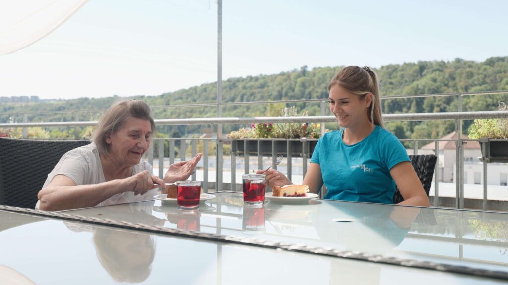 Seniorin und Pflegekraft genießen Kuchen und Tee auf der Dachterrasse der Demenz-WG Salucci in Esslingen